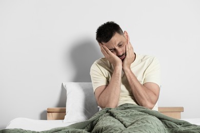 Photo of Sleep deprived man sitting on bed at home