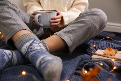 Photo of Woman relaxing with cup of hot winter drink on warm plaid indoors, closeup. Cozy season