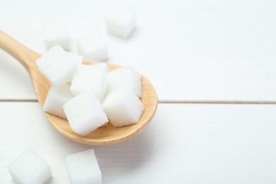 Photo of Many sugar cubes and wooden spoon on white table, closeup. Space for text