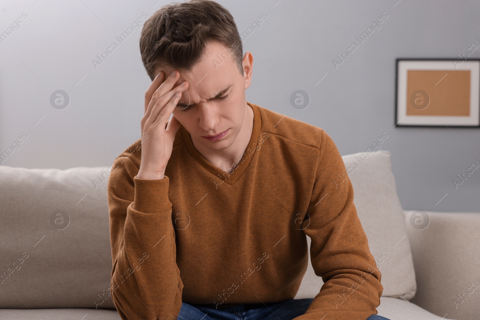 Photo of Sad man suffering from headache on sofa indoors