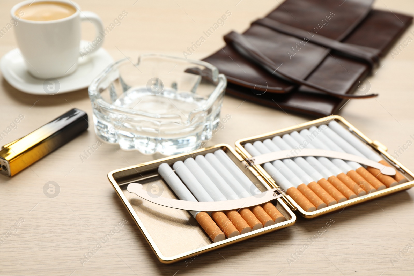 Photo of Open case with tobacco filter cigarettes, ashtray, clutch and lighter on wooden table