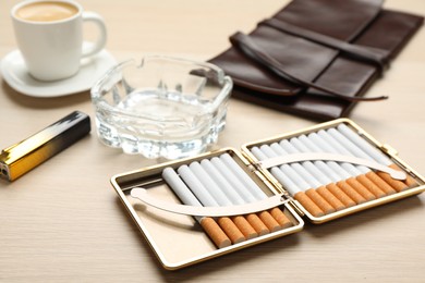 Photo of Open case with tobacco filter cigarettes, ashtray, clutch and lighter on wooden table