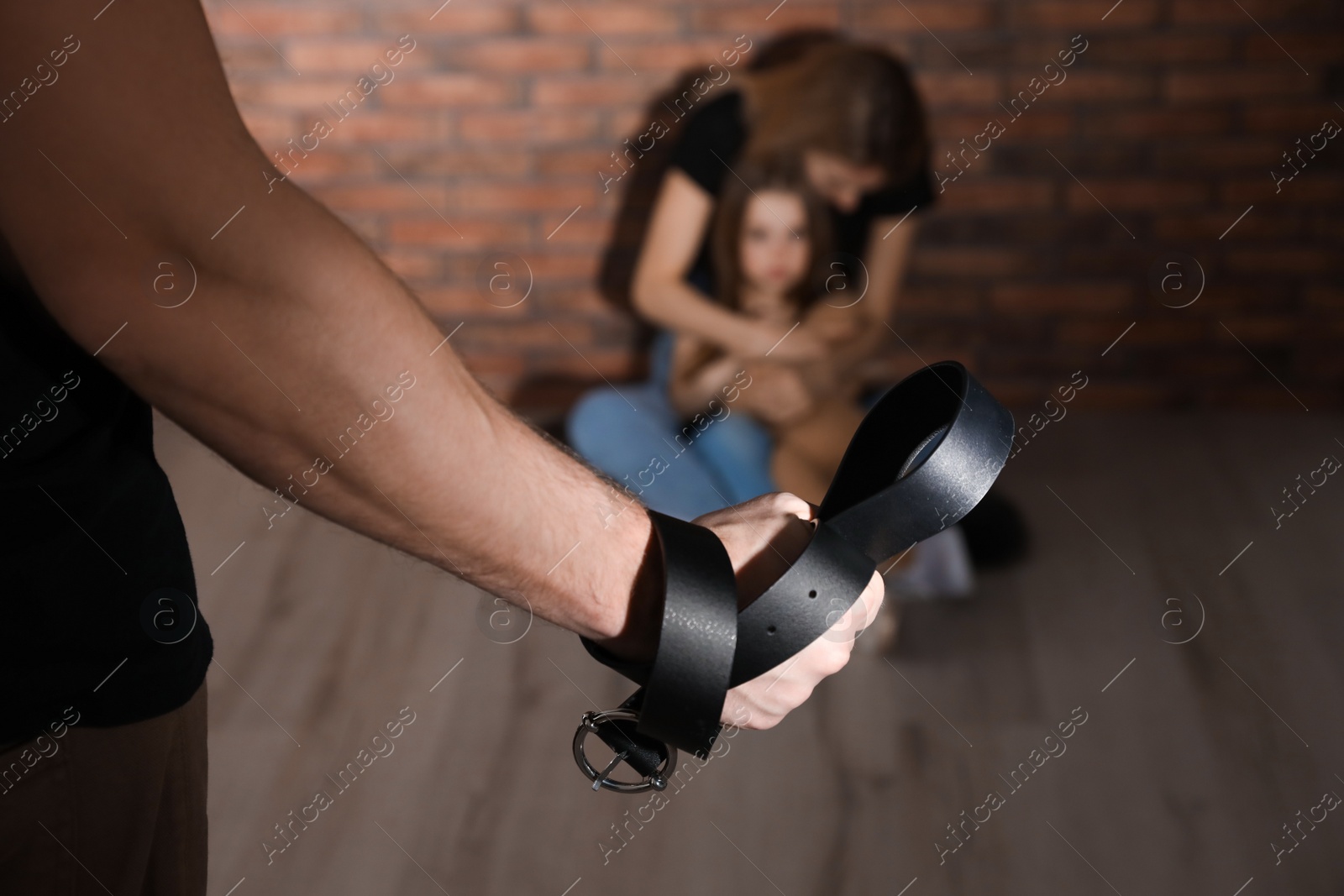 Photo of Man threatening his wife and daughter with belt indoors, closeup. Domestic violence