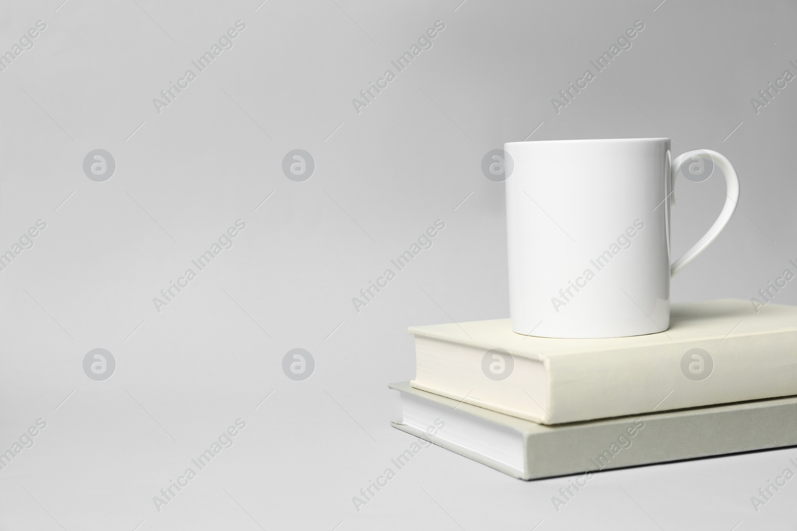 White ceramic mug and stack of books on light background, space for text Photo of White ceramic mug and stack of books on light background, space for text