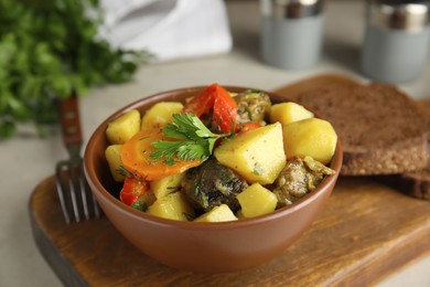 Photo of Tasty cooked dish with potatoes in earthenware on wooden board