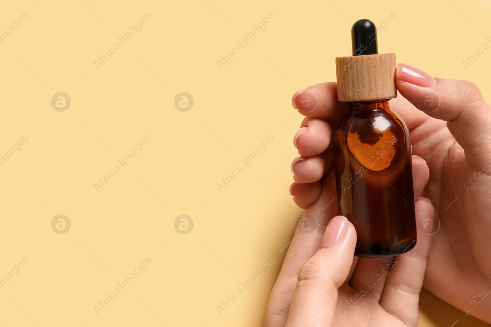 Photo of Woman holding bottle with serum on yellow background, closeup. Space for text