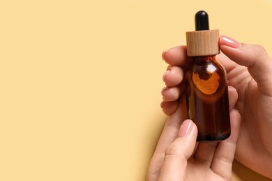 Woman holding bottle with serum on yellow background, closeup. Space for text