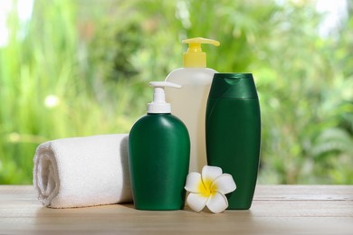 Photo of Different shower gel bottles with towel and plumeria flower on wooden table