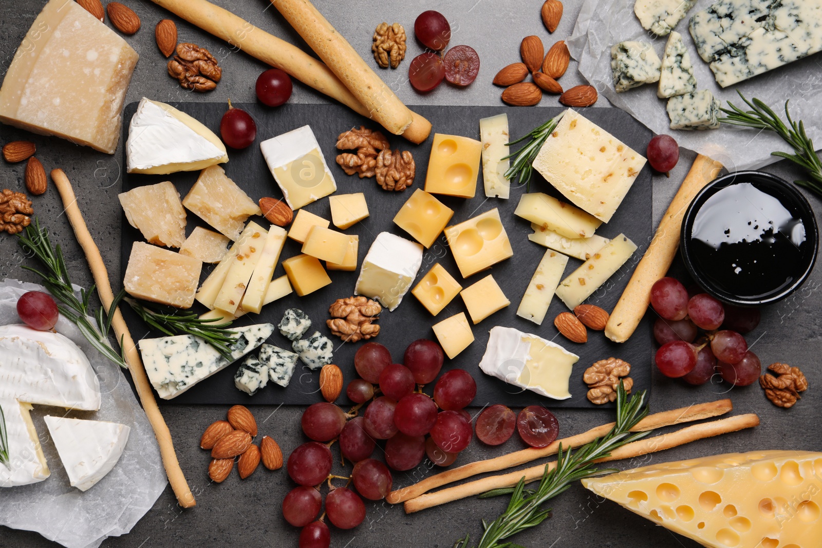 Photo of Cheese plate with grapes and nuts on dark table, flat lay