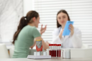 Endocrinologist examining patient at clinic, focus on model of thyroid gland, pills and blood samples in test tubes