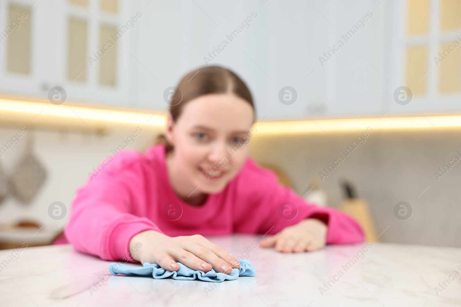 Photo of Woman cleaning white marble table with rag in kitchen, selective focus