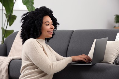 Photo of Happy young woman using laptop on sofa indoors