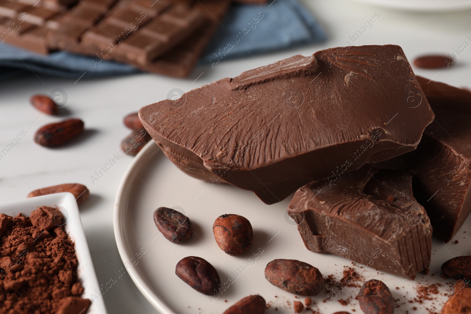 Photo of Pieces of tasty milk chocolate and cocoa beans on white table, closeup