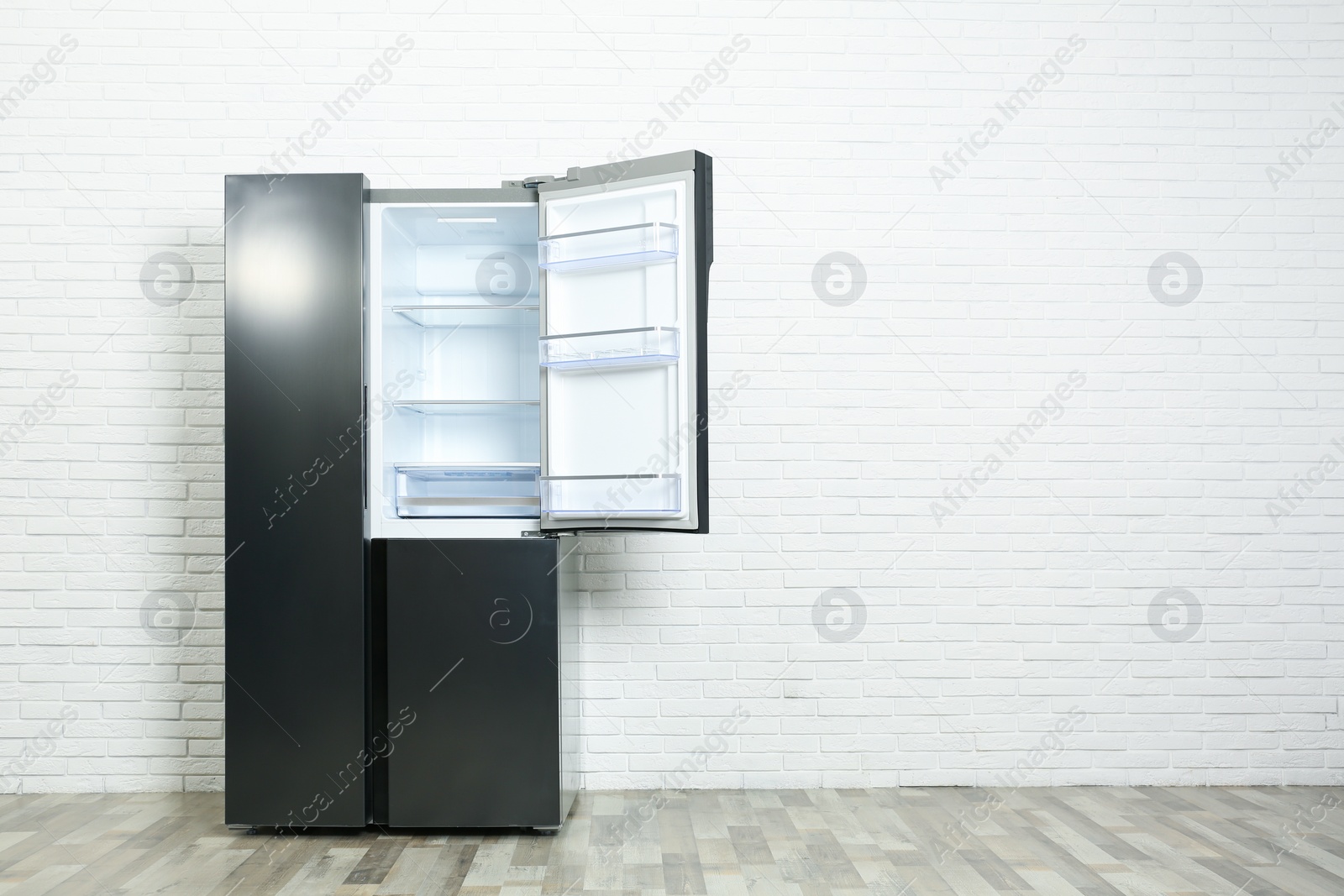 Photo of Modern empty refrigerator near white brick wall, space for text