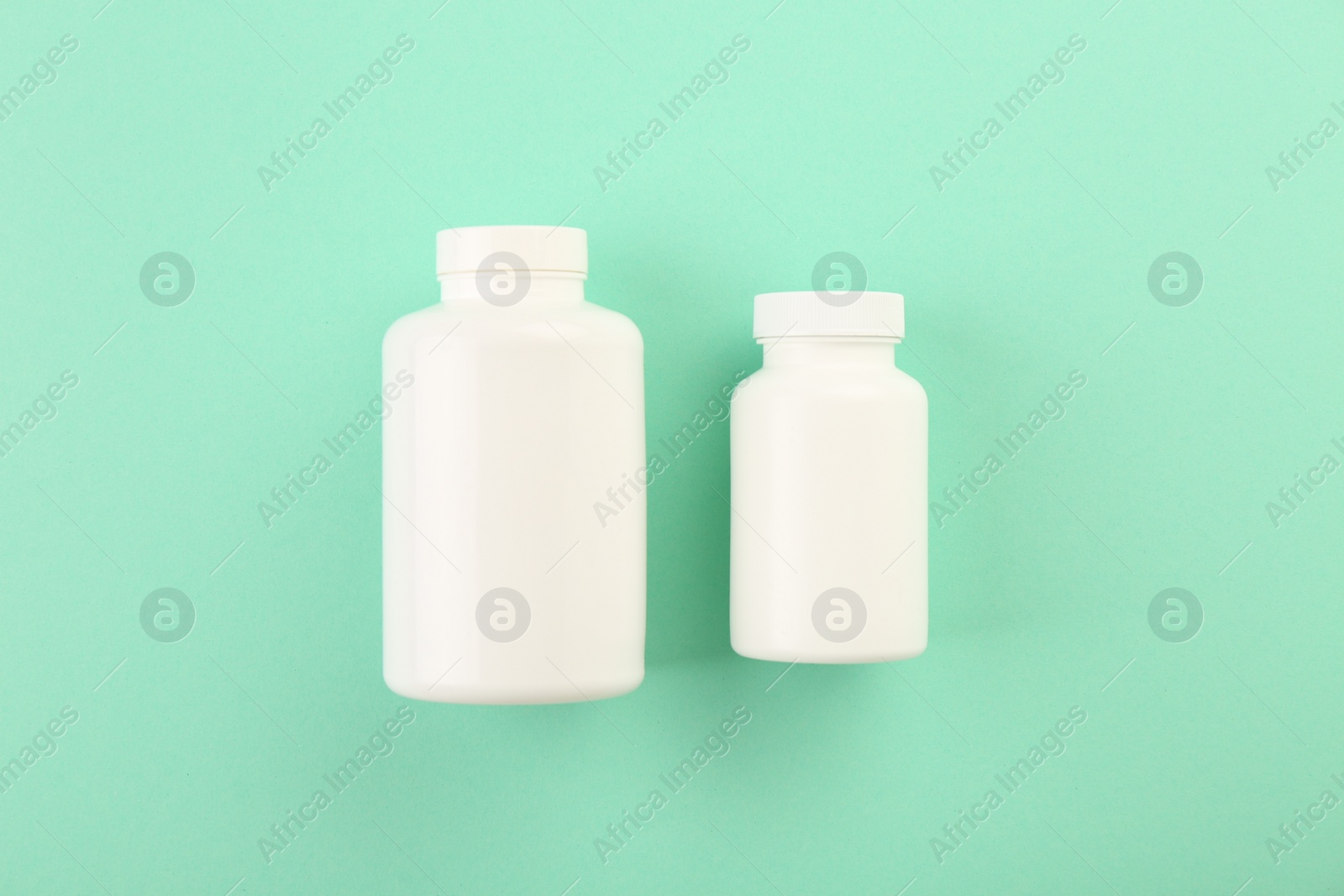 Photo of Blank white pill bottles on turquoise background, top view. Space for text