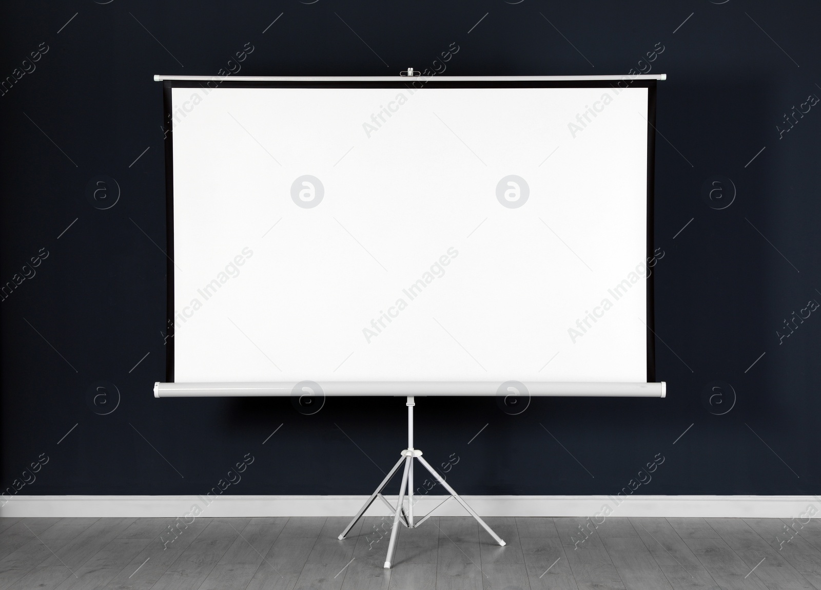 Photo of Blank projection screen near black wall indoors. Space for design