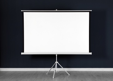Photo of Blank projection screen near black wall indoors. Space for design