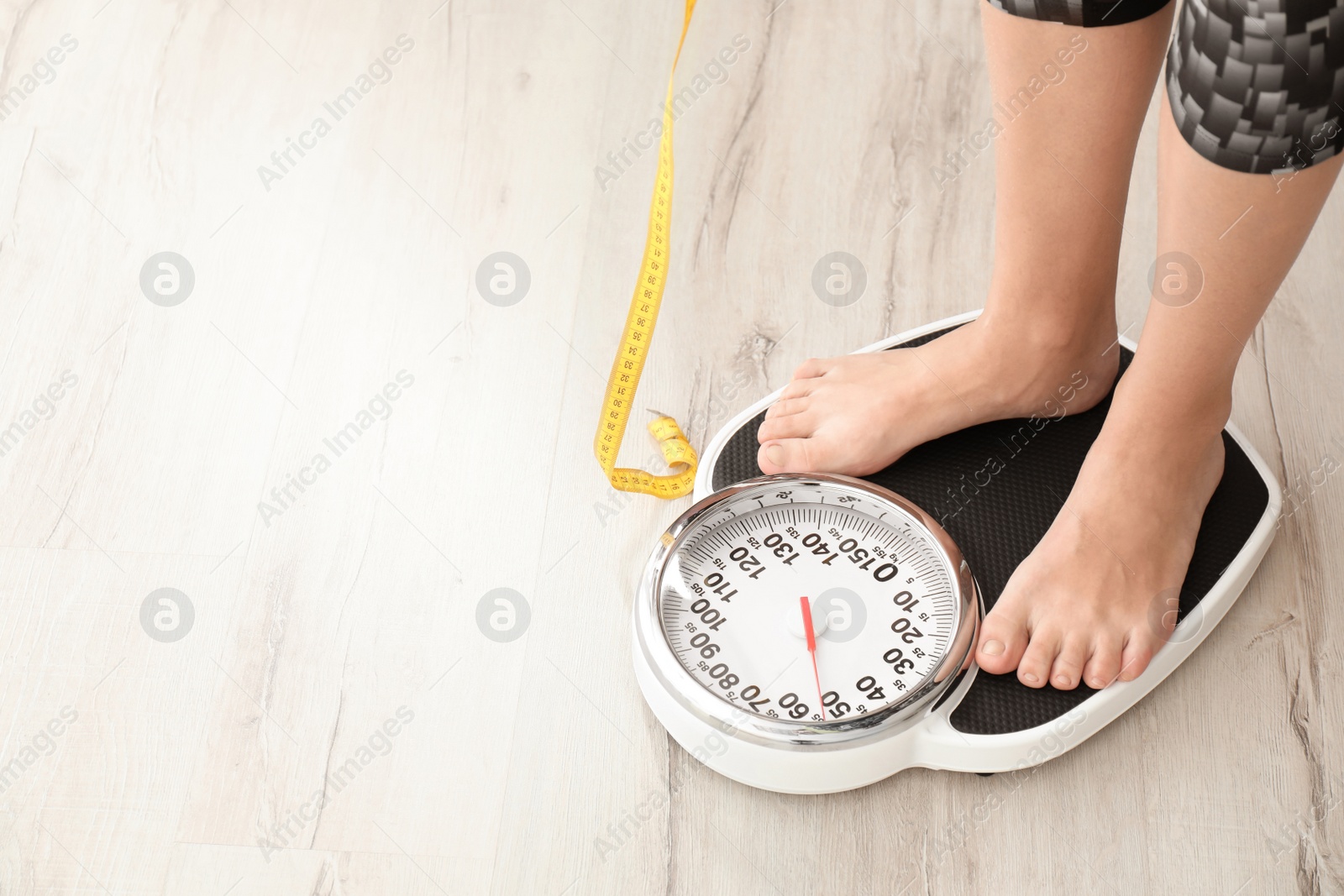 Photo of Woman with tape measuring her weight using scales on floor. Healthy diet