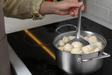 Photo of Woman cooking dumplings in saucepan with boiling water on cooktop, closeup