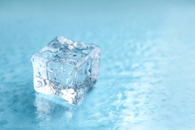 Photo of Crystal clear ice cube on light blue background, closeup. Space for text