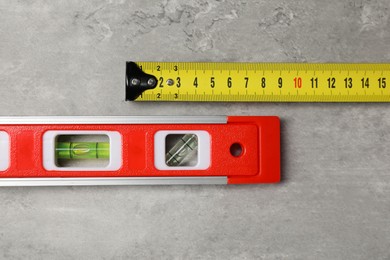 Building level and tape measure on grey table, top view