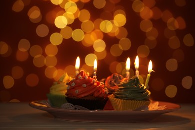 Plate with birthday cupcake on white table against blurred lights