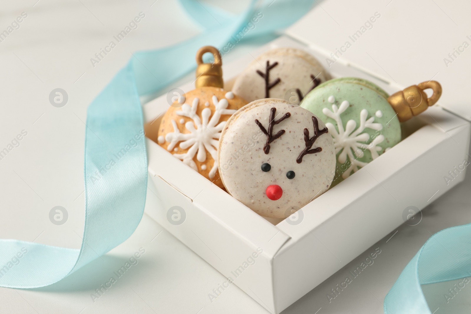 Photo of Beautifully decorated Christmas macarons in box and ribbon on white table, closeup