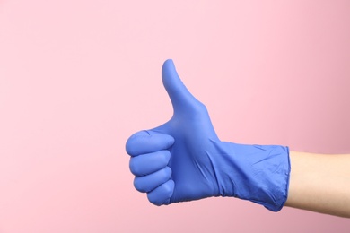Photo of Person in medical gloves showing thumb up on pink background, closeup of hand. Space for text