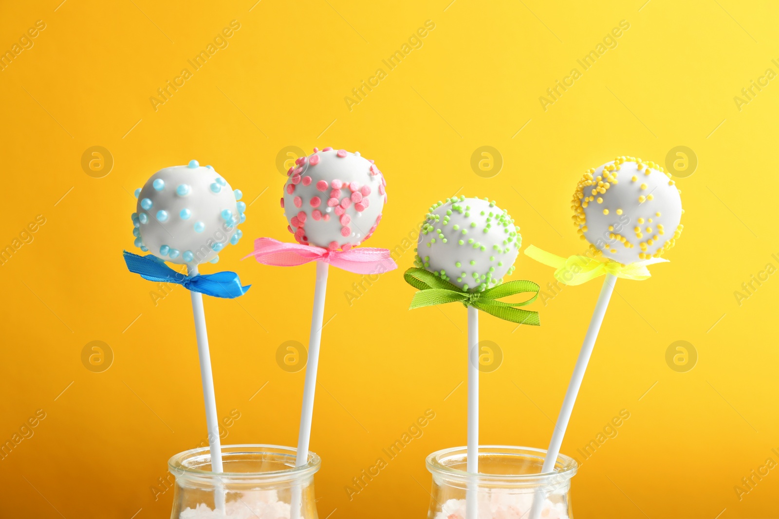 Photo of Tasty cake pops in glass bottles on yellow background