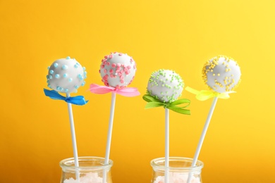 Photo of Tasty cake pops in glass bottles on yellow background