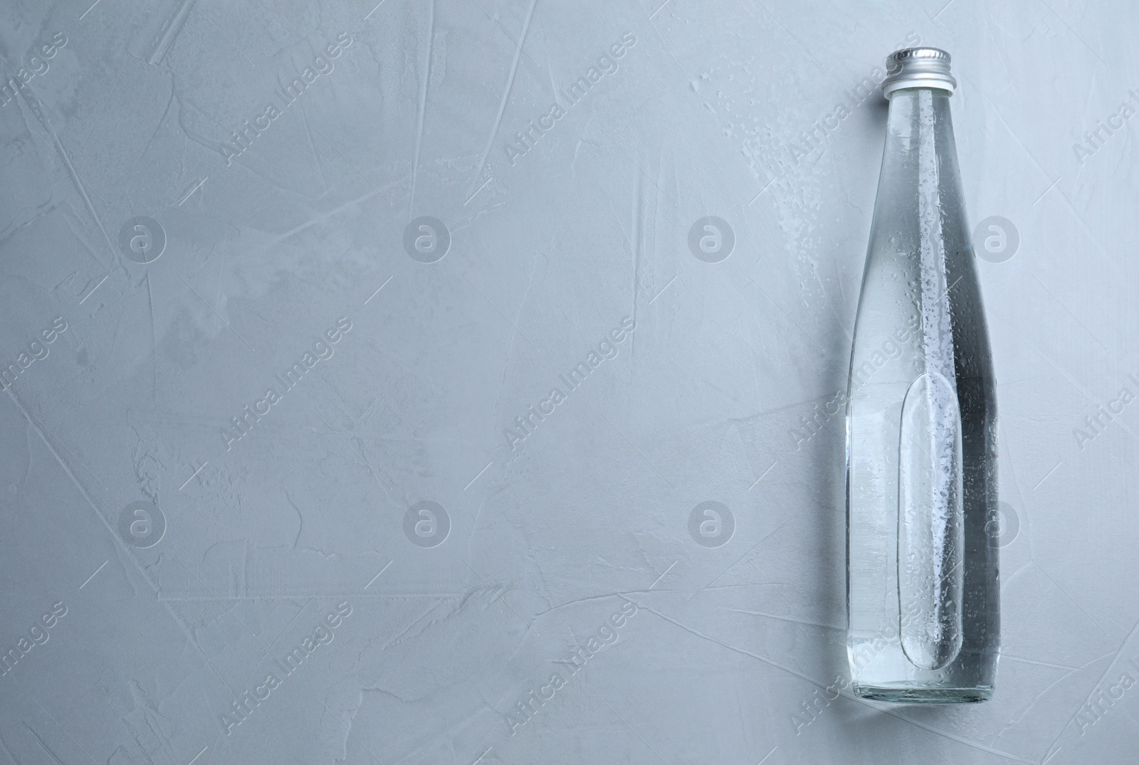 Photo of Glass bottle with water on light grey background, top view. Space for text