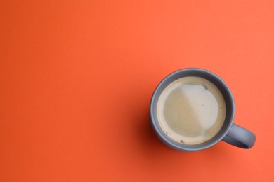 Photo of Grey mug of freshly brewed hot coffee on orange background, top view. Space for text