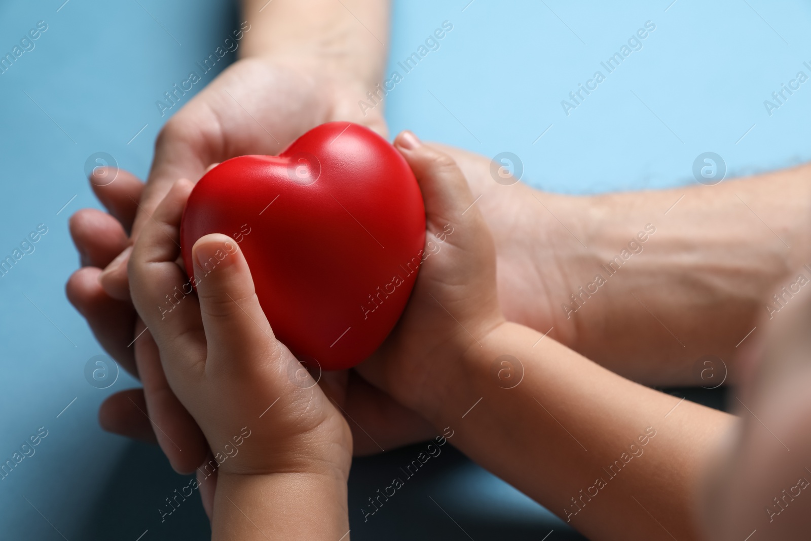 Photo of Father and his child holding red decorative heart on light blue background, closeup