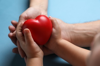 Photo of Father and his child holding red decorative heart on light blue background, closeup