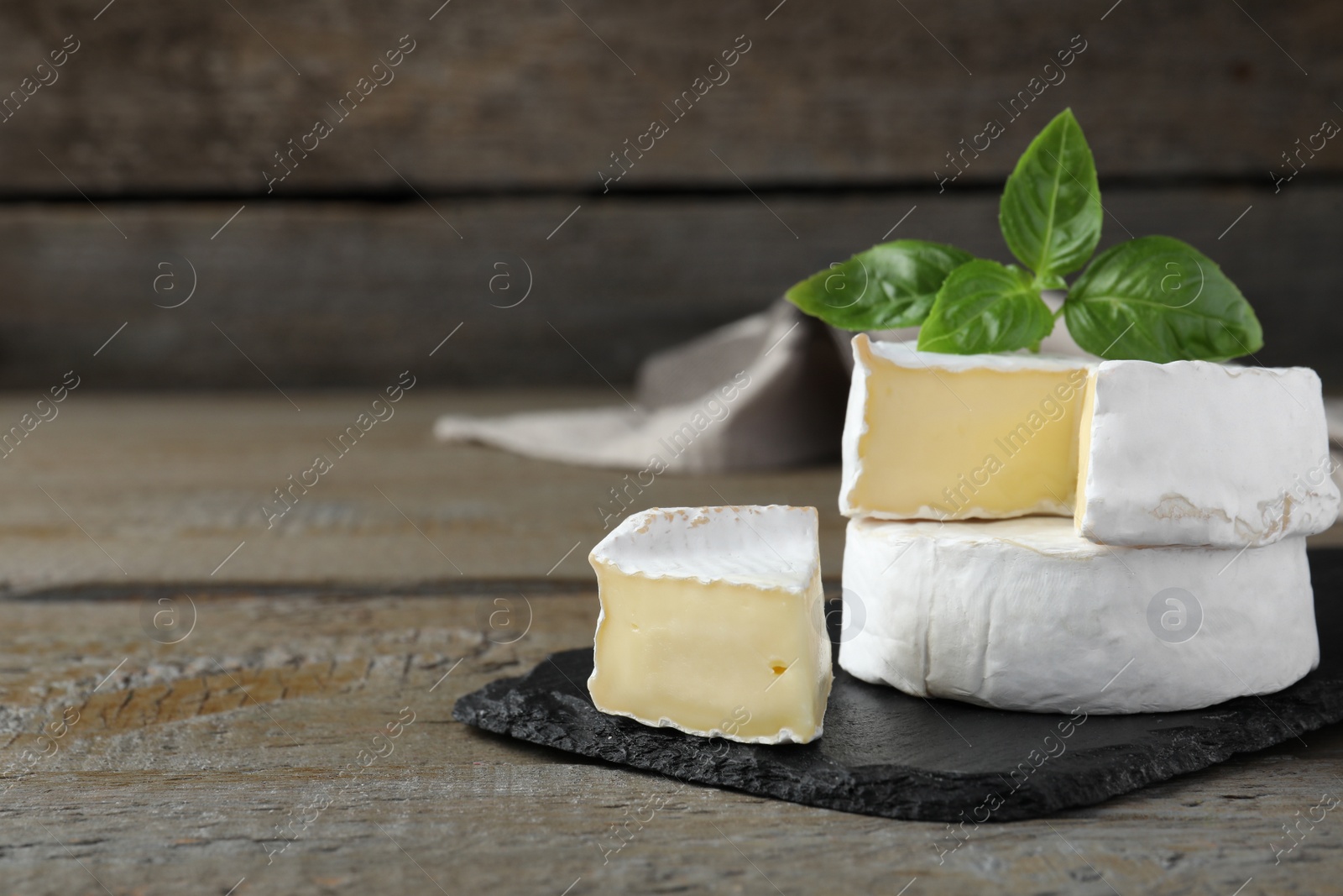 Photo of Tasty cut and whole brie cheeses with basil on wooden table, space for text