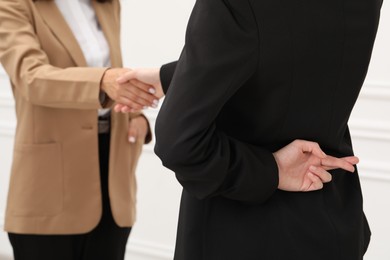 Photo of Employee crossing fingers behind her back while shaking hands with boss in office, closeup