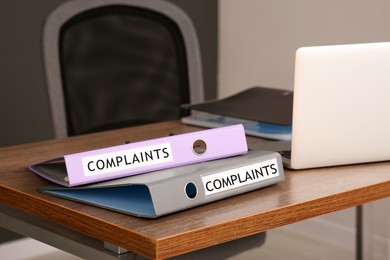 Folders with complaints labels near laptop on wooden table