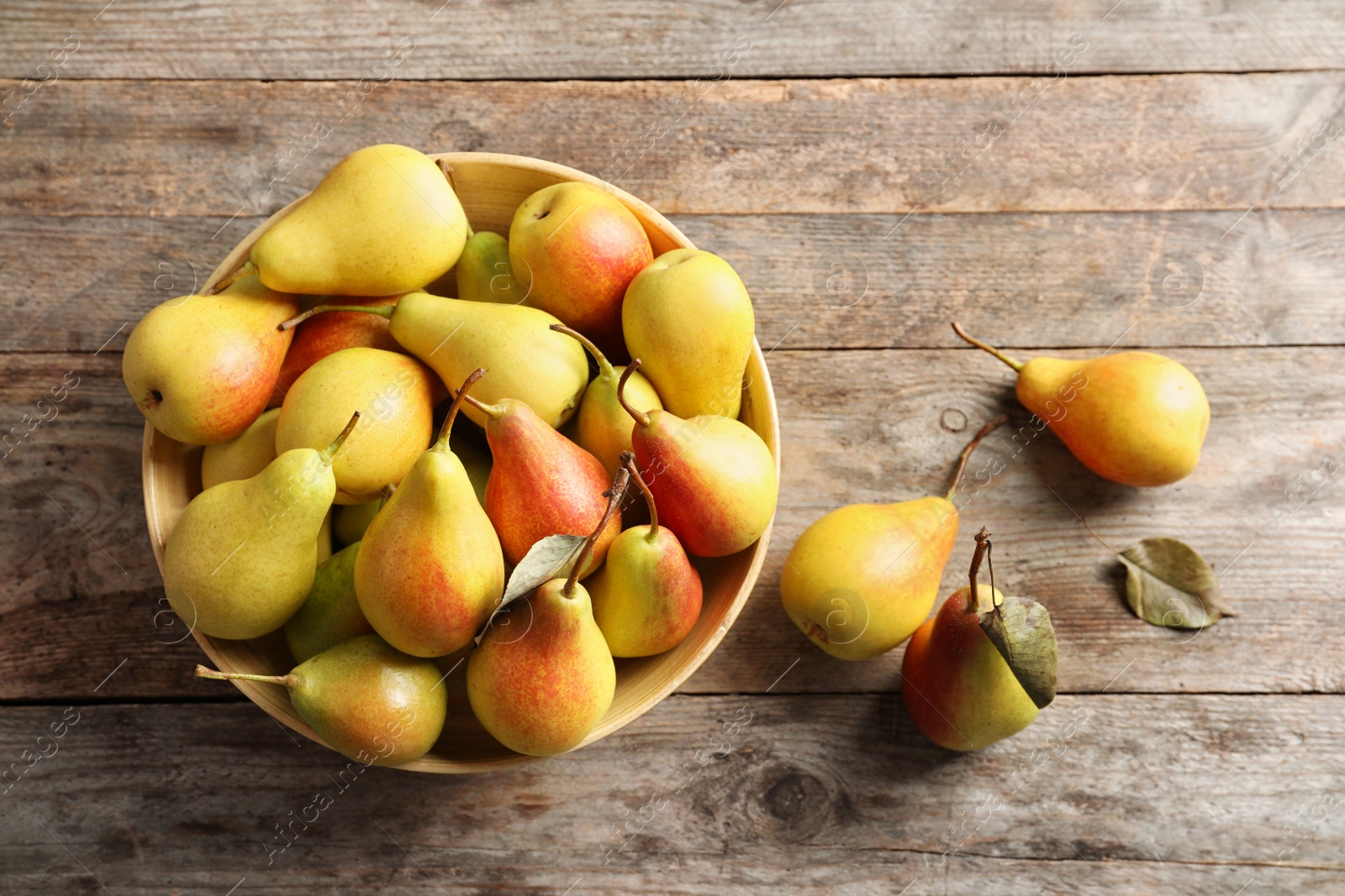 Photo of Bowl with ripe pears on wooden background, top view