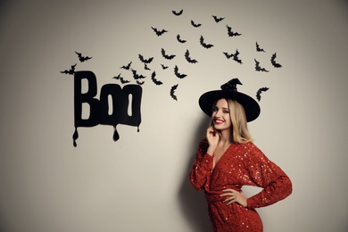 Woman in witch hat posing near white wall decorated for Halloween