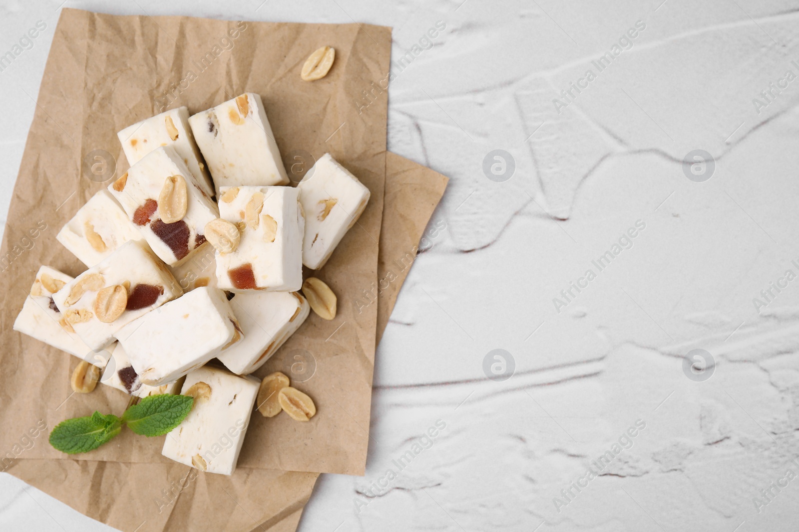 Photo of Pieces of delicious nutty nougat on white textured table, top view. Space for text