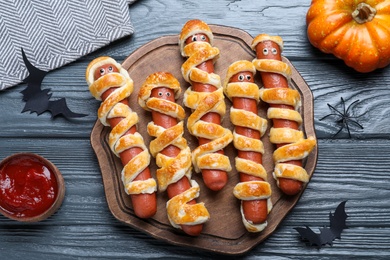 Photo of Cute sausage mummies served on wooden table, flat lay. Halloween party food