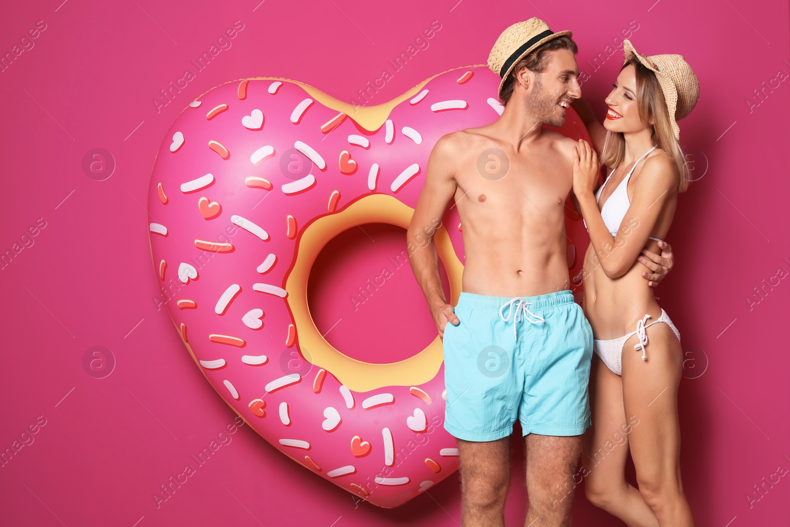 Photo of Happy young couple in beachwear with inflatable ring on color background