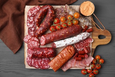 Different types of delicious sausages, sauce and tomatoes on black wooden table, flat lay