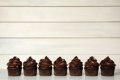 Photo of Delicious chocolate cupcakes with cream on white wooden table. Space for text