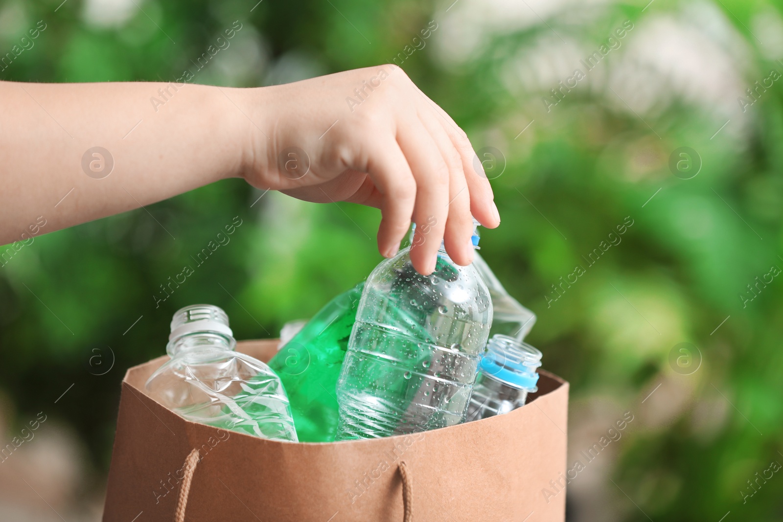 Photo of Woman putting used plastic bottle into paper bag on blurred background, closeup with space for text. Recycling problem