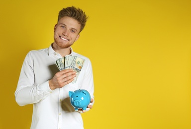 Photo of Young man with piggy bank and money on color background. Space for text