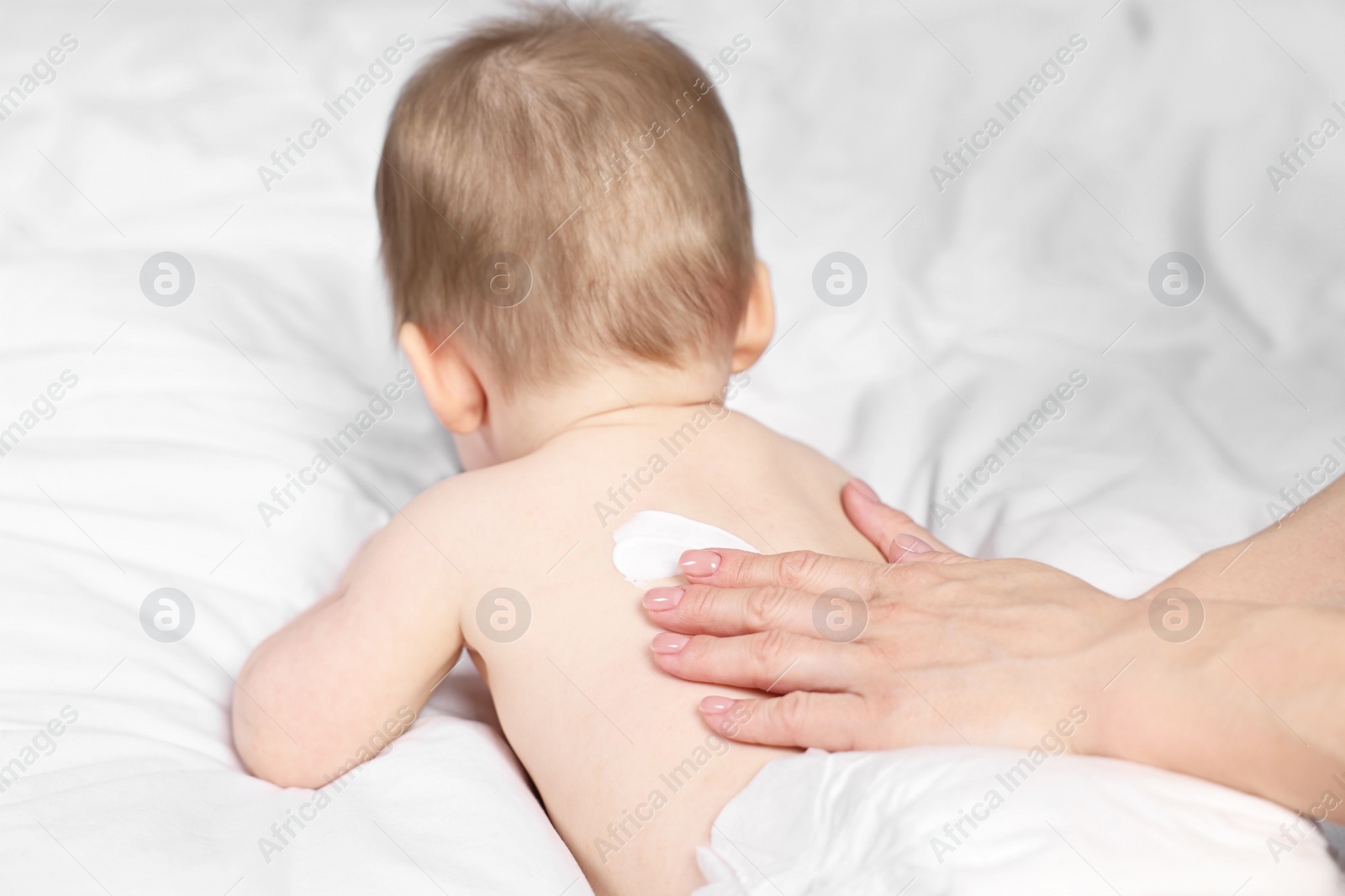 Photo of Woman applying body cream onto baby`s back on bed, closeup