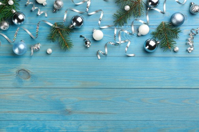 Photo of Shiny serpentine streamers, Christmas balls and fir branches on blue background, flat lay. Space for text