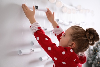 Photo of Little girl taking gift from Christmas advent calendar at home