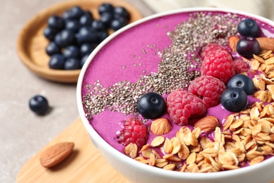 Delicious acai smoothie with berries and granola in bowl on table, closeup